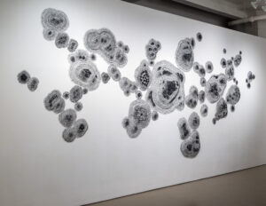 Photo of Rena Wood's artwork installed on a white gallery wall. Coiled Wire and hand-dyed vintage textiles.