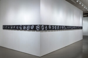 A long, black rectangular shape with white, amorphous embroidered shapes wraps around a white gallery wall corner.