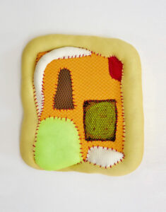 An abstract, fiber-filled, puffy fiber art piece made from peach, light yellow, fluoro green, dark green, red, and white pieces of fabric.